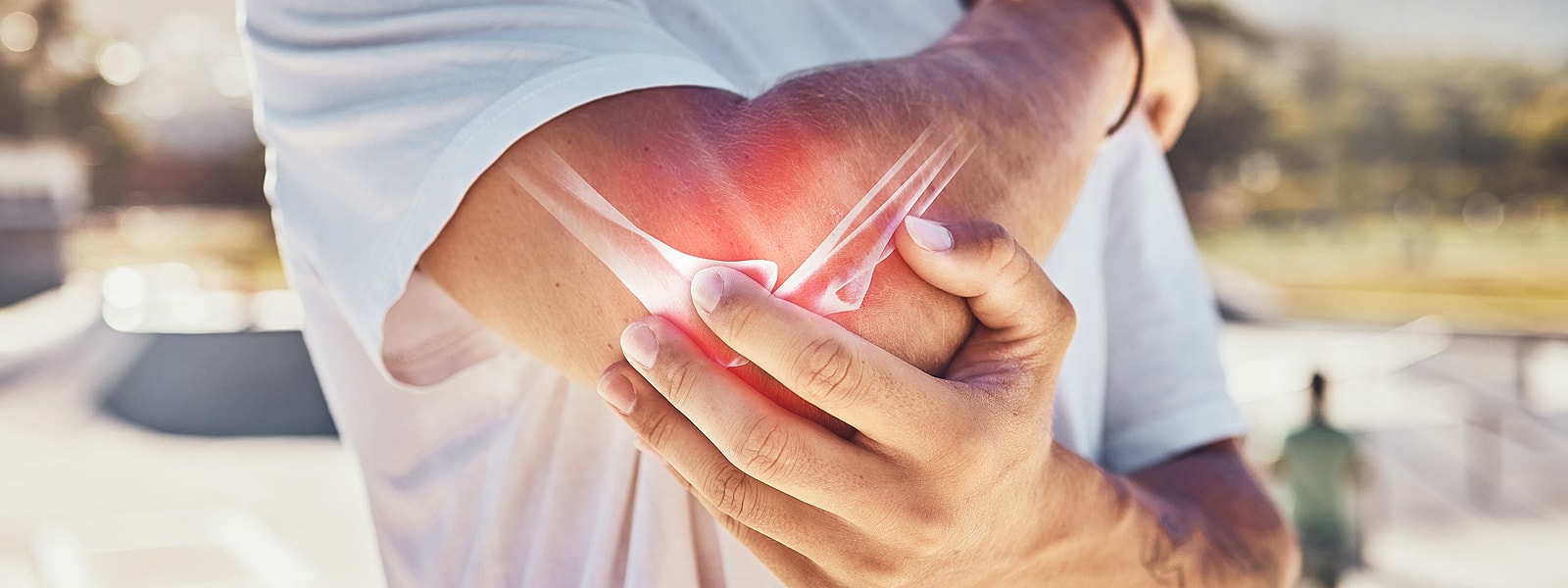 Person holding elbow in pain outdoors.