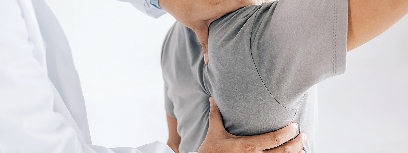Physician adjusting patient's shoulder in clinical setting